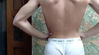 skinny boy flexes his muscles in underwear at home
